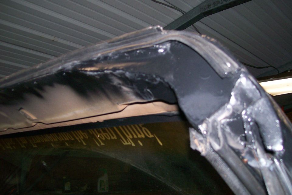 Underside of vehicle roof structure with welds and black paint. Yellow decal on rear window.