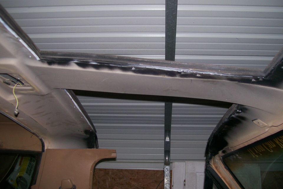 Tan truck cab with top removed showing freshly welded windshield header and roll bar hoop
