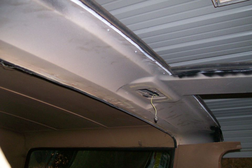 Interior view of vehicle roof, showing exposed wiring and sealant around sunroof.