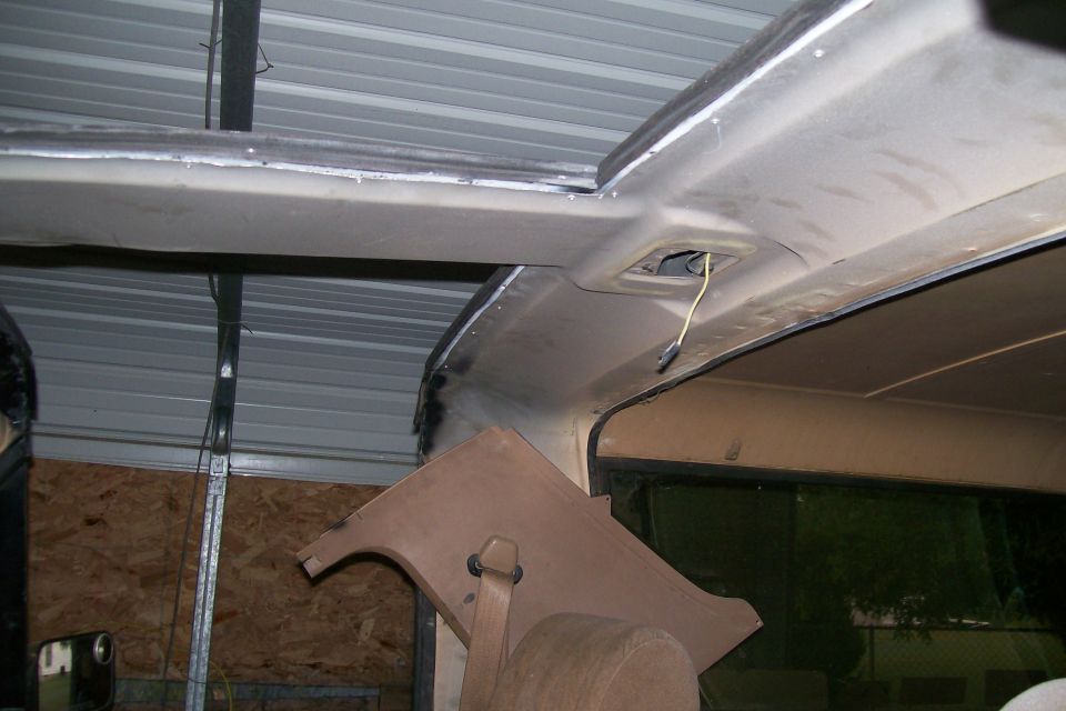 Bare-metal windshield header and roof rail inside a topless truck cab with hanging dome-light wire