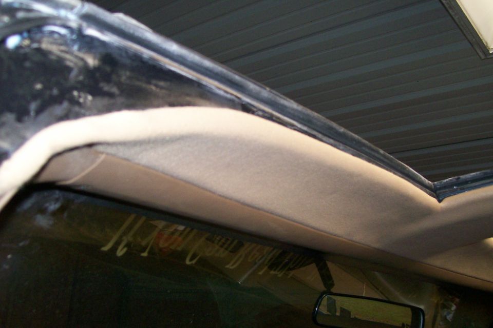 Tan windshield header trim and black weatherstrip inside a truck cab, rearview mirror below