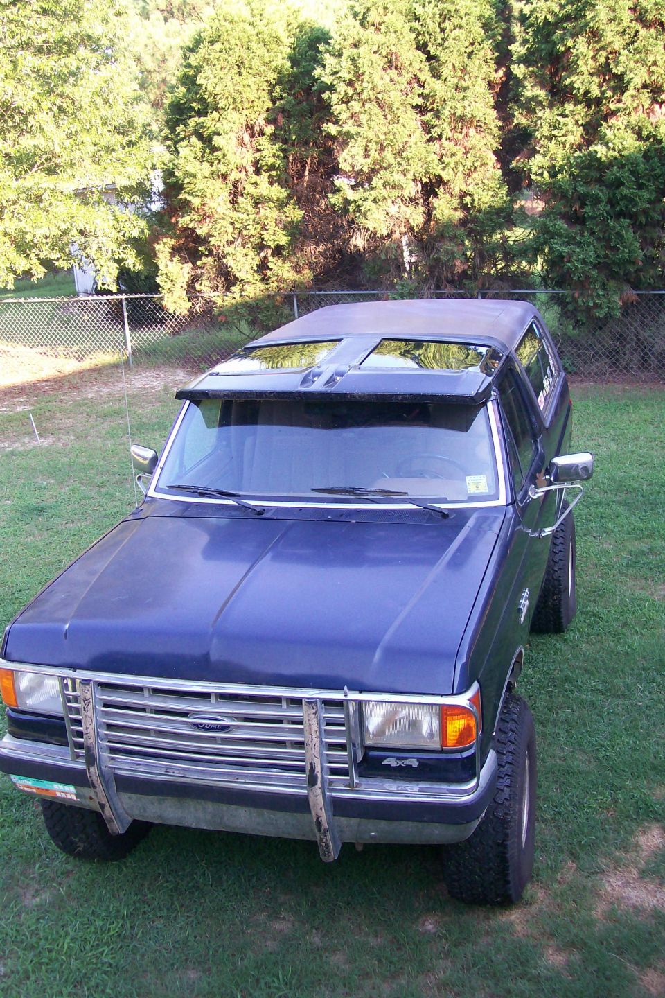 Dark blue Ford 4x4 SUV with chrome grille guard parked on grass by a chain-link fence
