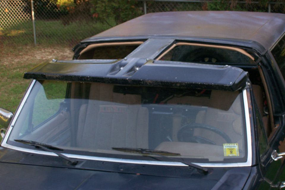 Dark SUV with roof panels lifted off, tan interior visible, parked by chain-link fence