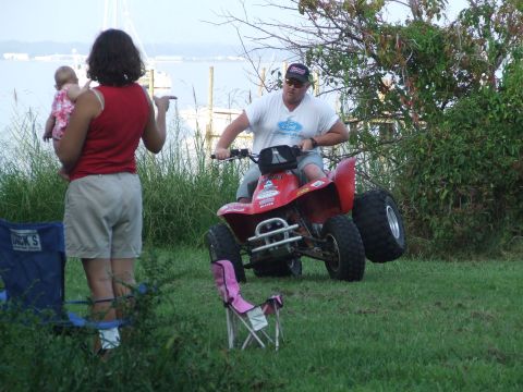 1967 Ford Bronco - A man rides a red ATV while a woman holds a baby nearby at an outdoor gathering.