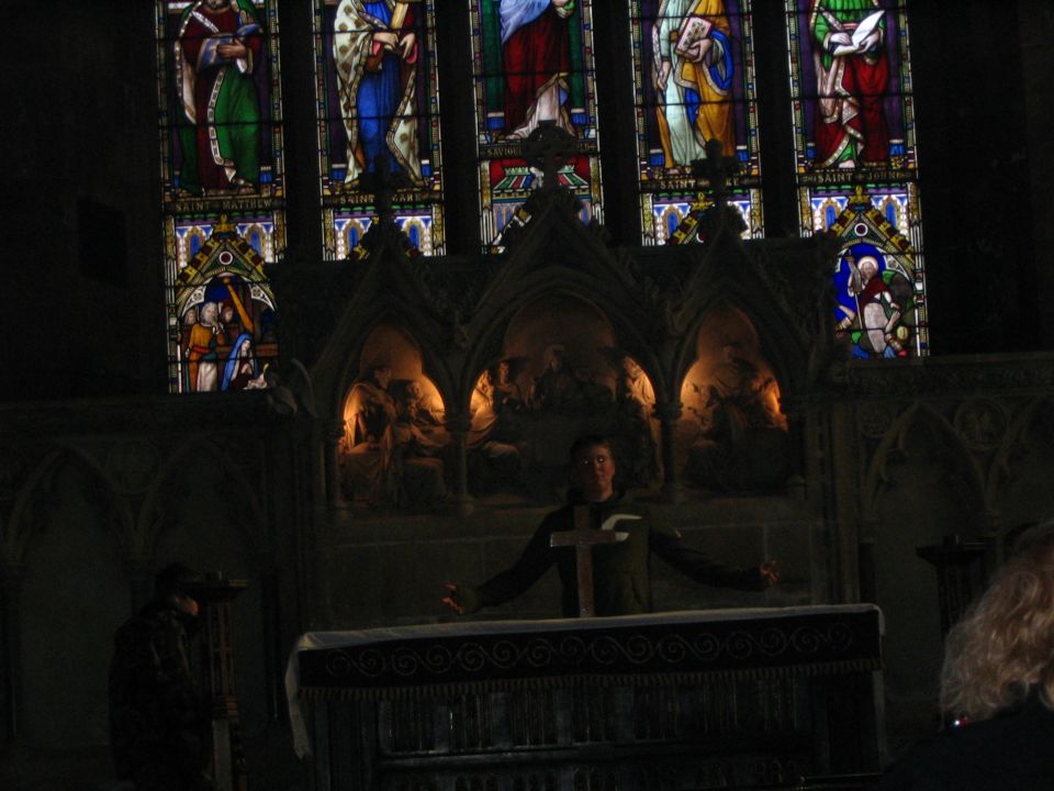 Interior of a church with stained glass windows and a person holding a cross at an altar