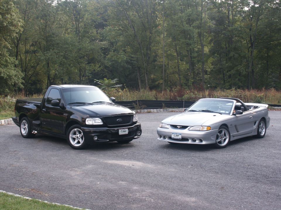 Black Ford F-150 Lightning pickup parked beside silver Mustang convertible