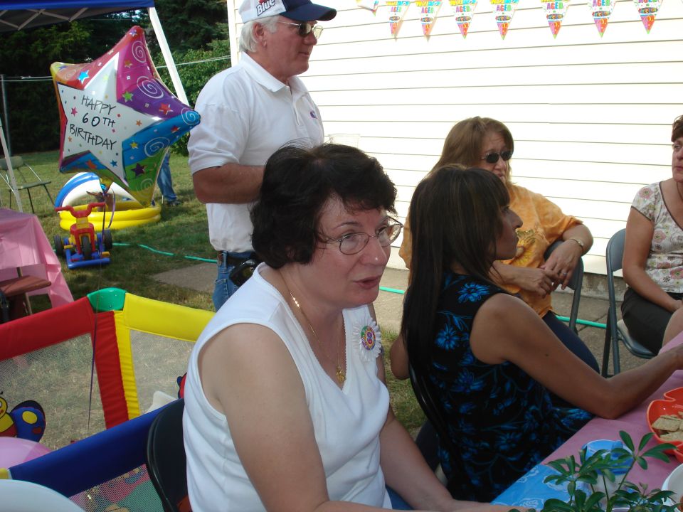 Birthday party scene with people gathered around a table, a balloon, and a bounce house