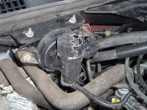 1999 Mercury Grand Marquis - Close-up of a damaged vacuum actuator component in an engine bay.