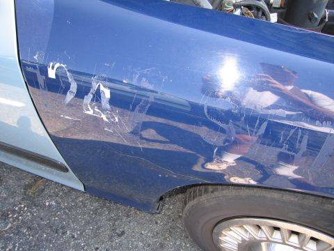 2001 Ford Crown Victoria - Scratched blue fender with partial white lettering visible.
