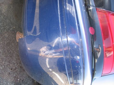 2001 Ford Crown Victoria - Close-up of a damaged blue car bumper and taillight, showing signs of wear and tear.