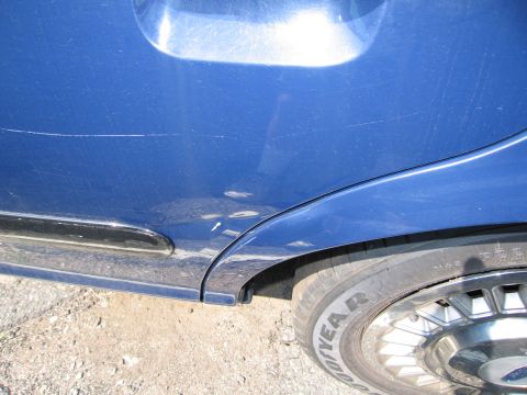 2001 Ford Crown Victoria - Scratches and a dent are visible on the blue paint of the car's side panel and fender.