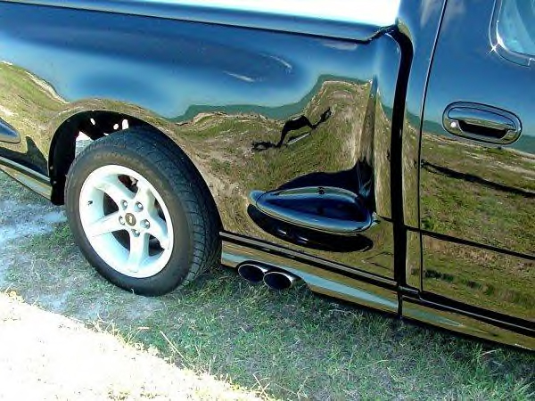 Black pickup side detail with dual side-exit chrome exhaust and 5-spoke silver wheel