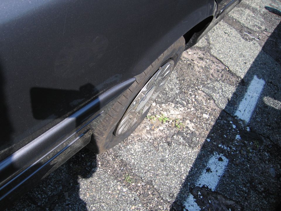 Dark colored car fender and wheel with a chrome hubcap visible