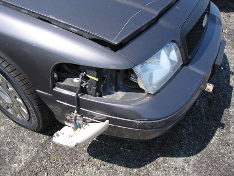 2001 Ford Crown Victoria - The front passenger side headlight assembly is detached from the vehicle, revealing wiring and mounting points.