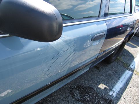 2001 Ford Crown Victoria - Deep scratches mar the side of a light blue vehicle parked outdoors.