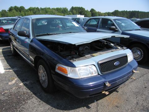 2001 Ford Crown Victoria - A two-tone Ford Crown Victoria sits in a lot with its hood open, revealing the engine compartment.