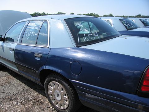 2001 Ford Crown Victoria - A two-tone blue Ford Crown Victoria is parked in a lot with other vehicles, showing writing on its windows.