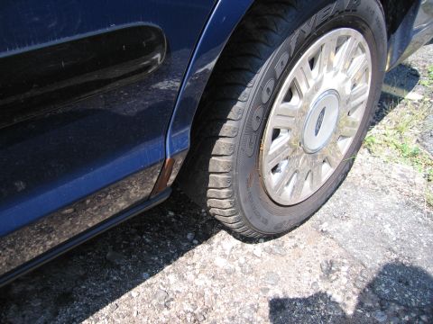 2001 Ford Crown Victoria - The rear wheel and lower body panel of a blue sedan are visible, with a Ford emblem on the hubcap.