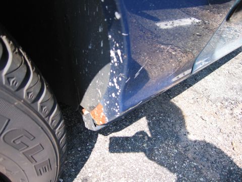 2001 Ford Crown Victoria - Close-up of a blue car's fender showing rust damage and white paint splatters.