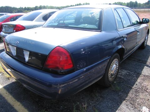 2001 Ford Crown Victoria - A blue police car is parked in a lot with other vehicles. Text is visible on the rear window.