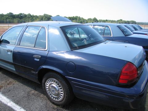 2001 Ford Crown Victoria - Several Ford Crown Victoria police cars are parked in a lot, one with its hood open and writing on the windows.