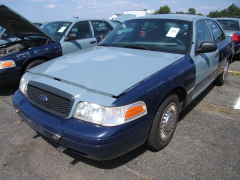 2001 Ford Crown Victoria - A two-tone Ford Crown Victoria is parked in a lot with other vehicles, some with hoods open.
