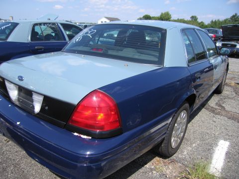 2001 Ford Crown Victoria - Two Ford Crown Victorias are parked in an outdoor lot, one in the foreground showing its rear quarter panel.
