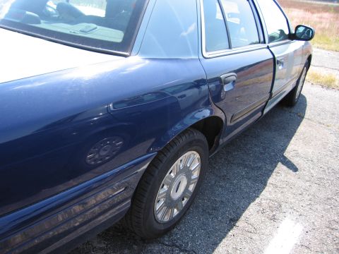 2001 Ford Crown Victoria - The rear quarter panel and door of a blue 2001 Ford Crown Victoria are visible from a side angle.