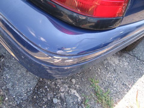 2001 Ford Crown Victoria - Close-up of the rear bumper and taillight of a blue 2001 Ford Crown Victoria, showing some damage to the bumper.