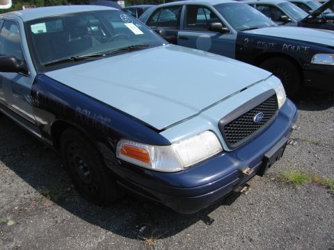 2001 Ford Crown Victoria - A police car with a two-tone paint scheme sits in a lot with other vehicles behind it.