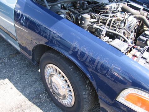 2001 Ford Crown Victoria - The fender of a blue police car displays "U.S. POLICE" text, with the hood open revealing the engine compartment.