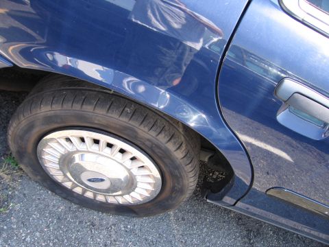 2001 Ford Crown Victoria - Close-up of the rear wheel and door of a blue sedan, showing the Ford logo on the hubcap.