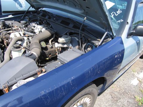 2001 Ford Crown Victoria - The engine bay and fender of a blue and light blue police car are visible with the hood open.