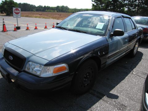 2001 Ford Crown Victoria - A two-tone Ford Crown Victoria is parked in an outdoor lot with traffic cones and a sign in the background.