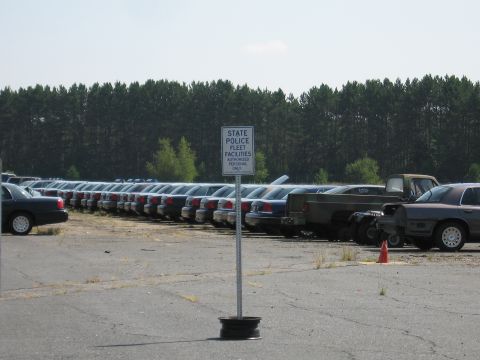 2001 Ford Crown Victoria - A large lot filled with Ford Crown Victoria police cars, marked with a sign for authorized personnel only.