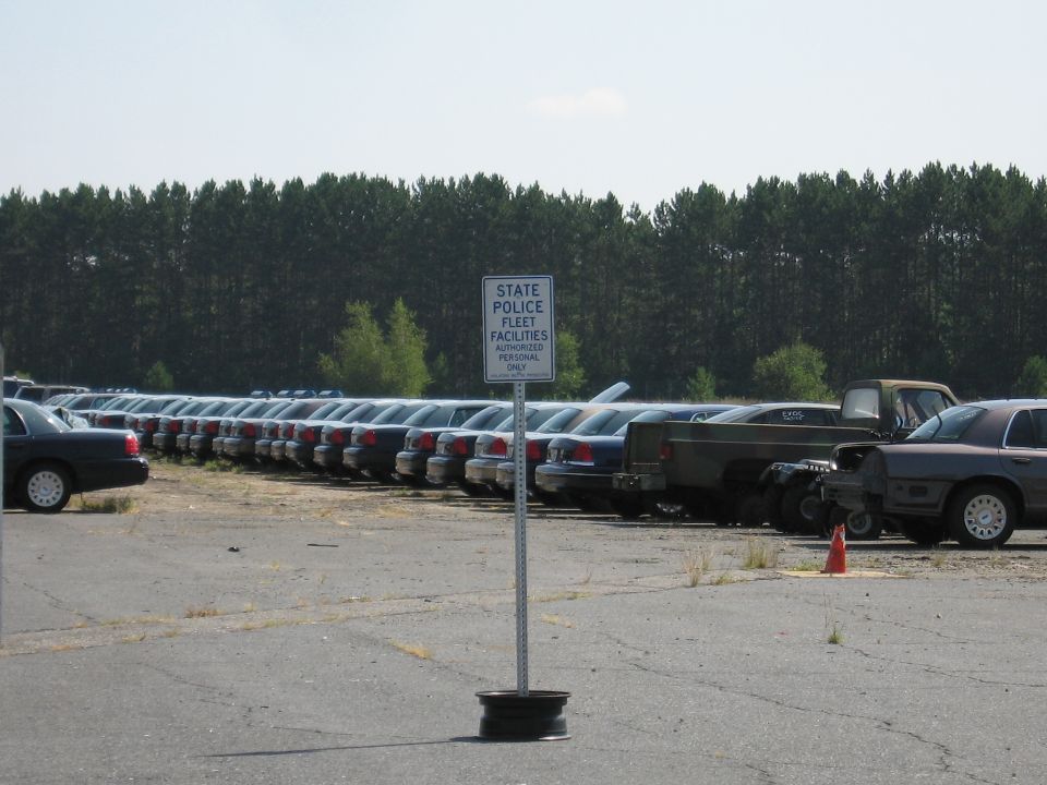 Rows of Ford Crown Victoria police cars parked in a lot, with a sign for State Police Fleet Facilities
