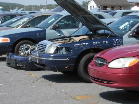 2001 Ford Crown Victoria - Several police cars are parked in a lot, one with its hood open and front bumper removed.