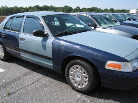 2001 Ford Crown Victoria - A two-tone Ford Crown Victoria, possibly a former police vehicle, is parked in a lot with other cars.