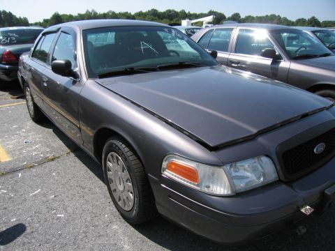 2001 Ford Crown Victoria - Dark gray 2001 Ford Crown Victoria with hood ajar, parked outdoors with other vehicles.