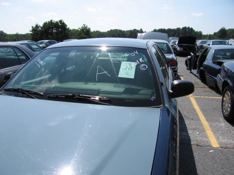 2001 Ford Crown Victoria - A light blue sedan is parked in a lot with other vehicles. Writing is visible on the windshield.