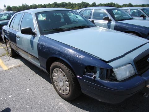 2001 Ford Crown Victoria - A two-tone Ford Crown Victoria sits in a parking lot, showing damage to its front end.