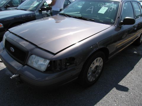 2001 Ford Crown Victoria - A gray 2001 Ford Crown Victoria is seen from the front with one headlight missing and a paper tag on the windshield.