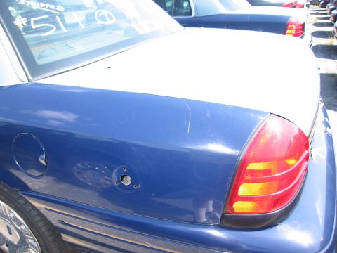 2001 Ford Crown Victoria - A blue and white sedan is seen from the rear quarter panel, with another similar vehicle in the background.
