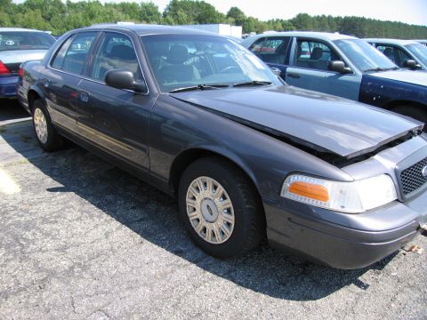 2001 Ford Crown Victoria - A dark gray Ford Crown Victoria is parked in a lot with its hood open, showing other vehicles nearby.