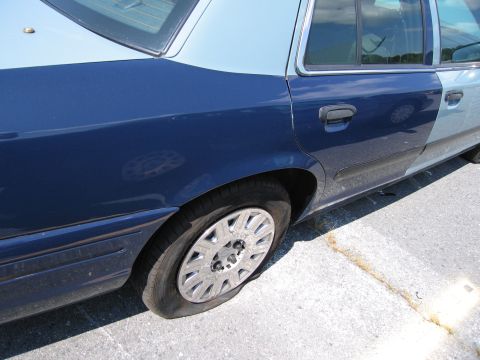 2001 Ford Crown Victoria - A two-tone blue sedan, possibly a 2001 Ford Crown Victoria, is parked with a flat rear tire.