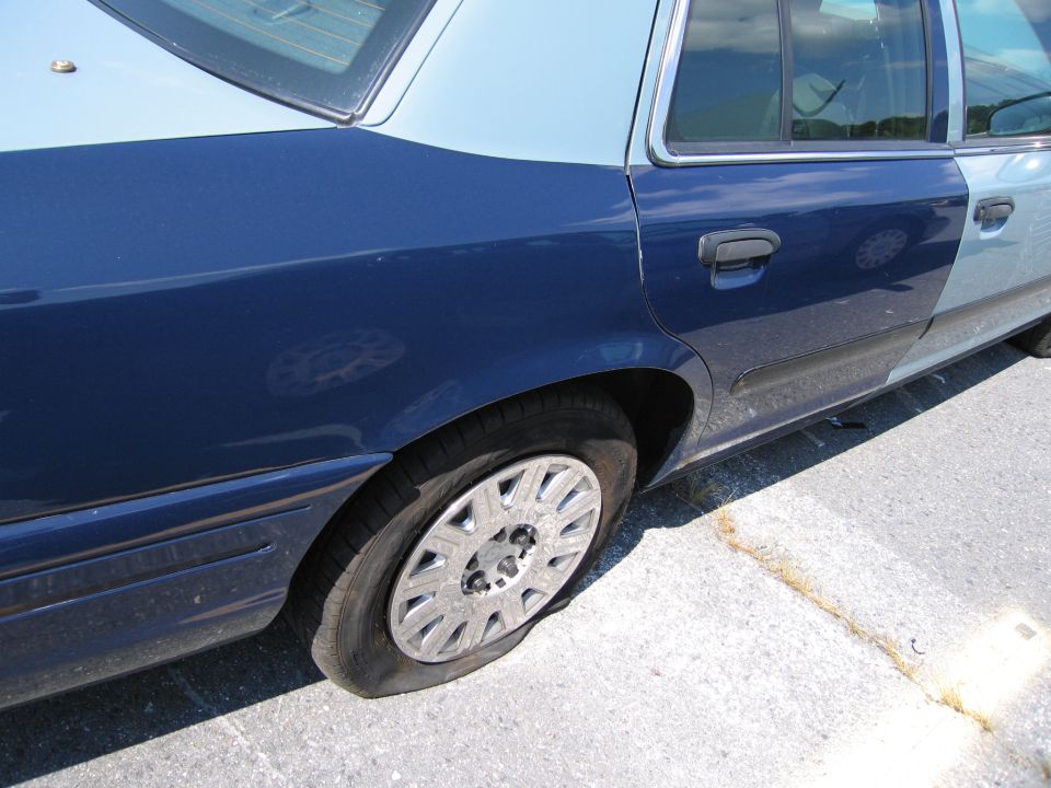 Two-tone blue sedan with a flat rear tire, seen from the side