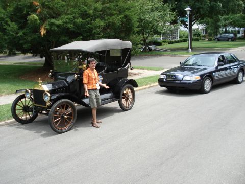 Person standing next to a 1915 Ford Model T touring car. A modern police car is parked behind it
