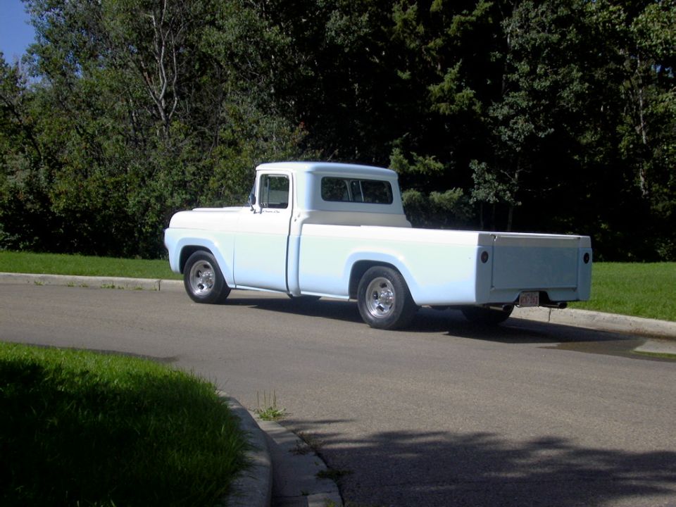 Light blue classic pickup truck, rear three-quarter view, parked on a street near trees