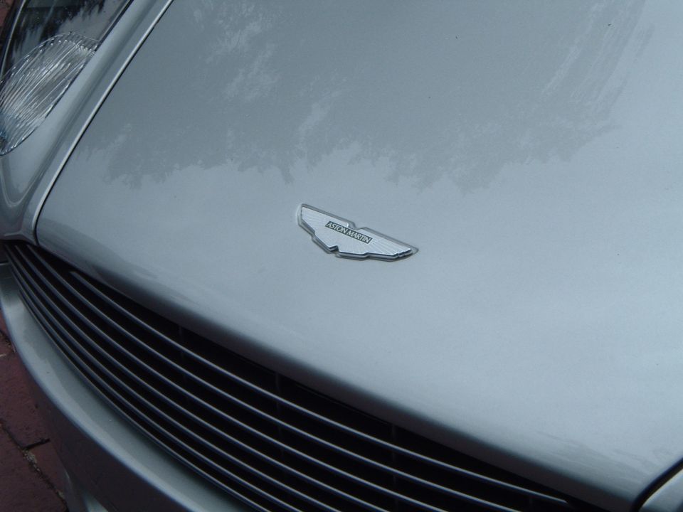 Close-up of Aston Martin hood emblem and grille on a silver car