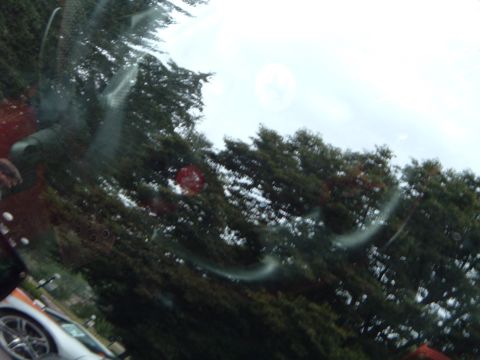 1999 Mercury Grand Marquis - A silver car is visible from the side, seen through a dirty windshield with trees in the background.